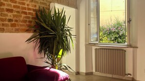 Une pièce avec un mur en briques, un canapé rouge, une grande plante en pot et une fenêtre donnant sur un paysage verdoyant.