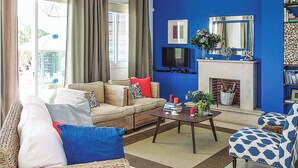 A living room with a sofa, armchairs, a coffee table, a fireplace, and a television. - Villa Elena Coral (Pegeia)