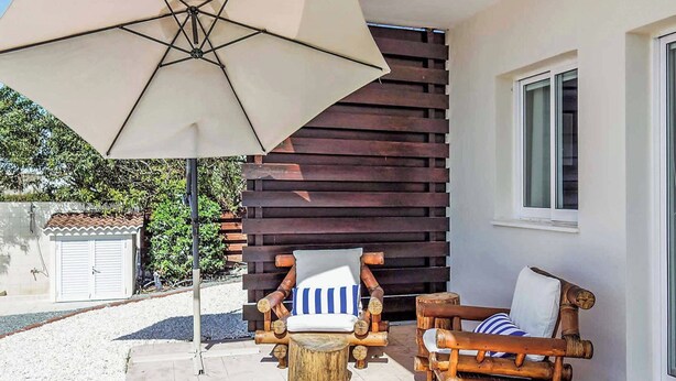 A patio with two wooden chairs, a small wooden stool, and a large umbrella. - Villa Elena Coral (Pegeia)