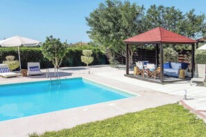 Ein rechteckiger Swimmingpool mit Holzdeck, Liegestühlen und einem Pavillon.