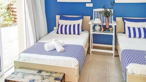 A room with two beds, each with blue and white striped bedding, a small table with a vase, and a chair. - Villa Elena Coral (Pegeia)