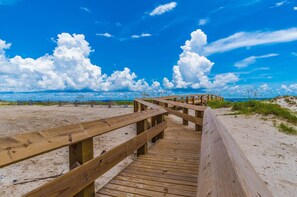 A wooden boardwalk leading to a beach with a clear blue sky and clouds.