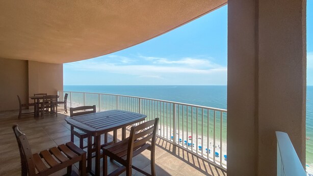 Ein Balkon mit Holztisch und -stühlen, der auf einen Strand mit freiem Blick aufs Meer blickt.