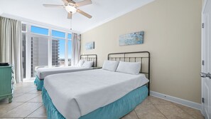 A hotel room with two beds, a ceiling fan, a view of the city, and a painting on the wall.