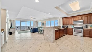 A spacious kitchen with a large island, wooden cabinets, and modern appliances. There is a dining area with a view of the ocean. - Beachfront 4BR Corner Unit! Water Slide!! (Gulf Shores)
