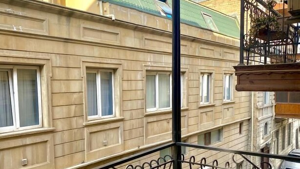 Un balcon avec une rambarde en métal, une vue sur les immeubles voisins et une voiture garée.