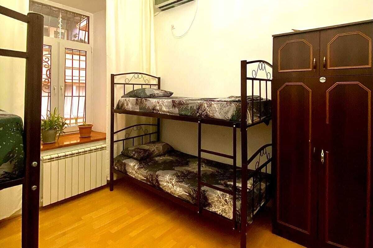 A room with a bunk bed, a wardrobe, a radiator, and a window with curtains.