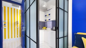Une cuisine moderne avec des meubles blancs, un appareil électroménager jaune et une cloison en verre à cadre bleu.