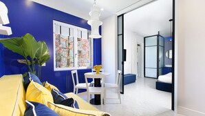 Un salon moderne avec un mur d’accent bleu, un canapé jaune et un coin repas comprenant une table et des chaises blanches.