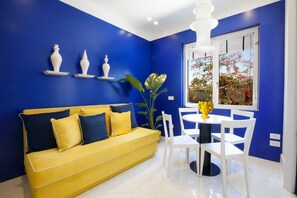 Ein Zimmer mit einem gelben Sofa, weißen Stühlen und einer blauen Akzentwand.