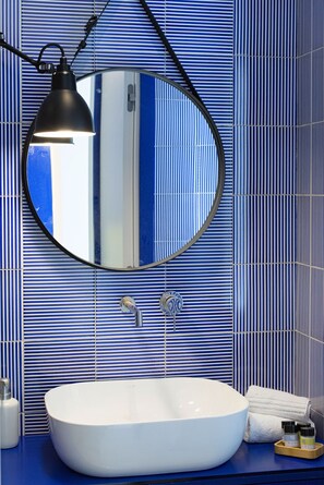 Ein Badezimmer mit einem weißen, ovalen Waschbecken, einem runden Spiegel und einer schwarzen Pendelleuchte.