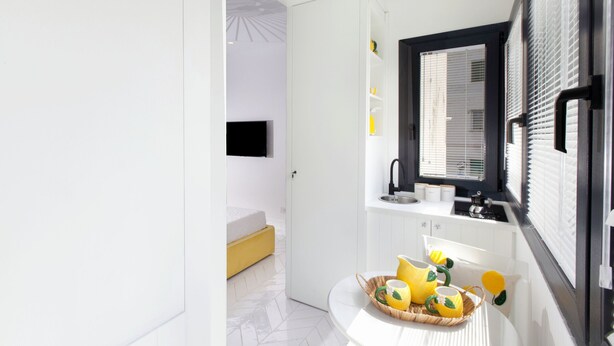 Une salle de bain moderne avec un meuble-lavabo blanc, un miroir et un évier. La pièce adjacente contient un lit jaune.