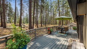 A wooden deck with a table and chairs, surrounded by tall trees. - New! Hot Tub ~ Heart of Sunriver ~  Fireplace ~ Updated Home ~ SHARC passes! (Sunriver)