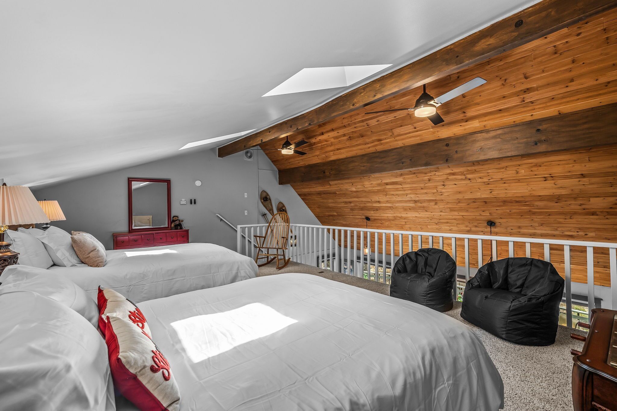 A bedroom with two beds, a wooden ceiling, a balcony with a railing, and a chair.