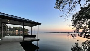 Um pavilhão à beira-mar com um banco, com vista para um lago calmo e um pôr do sol ao fundo.