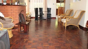 A room with a brick fireplace, wooden flooring, and wicker chairs. - Tranquil homestays (Naro Moru)