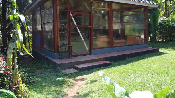 A glass-walled structure with a tiled roof, surrounded by greenery. - Tranquil homestays (Naro Moru)