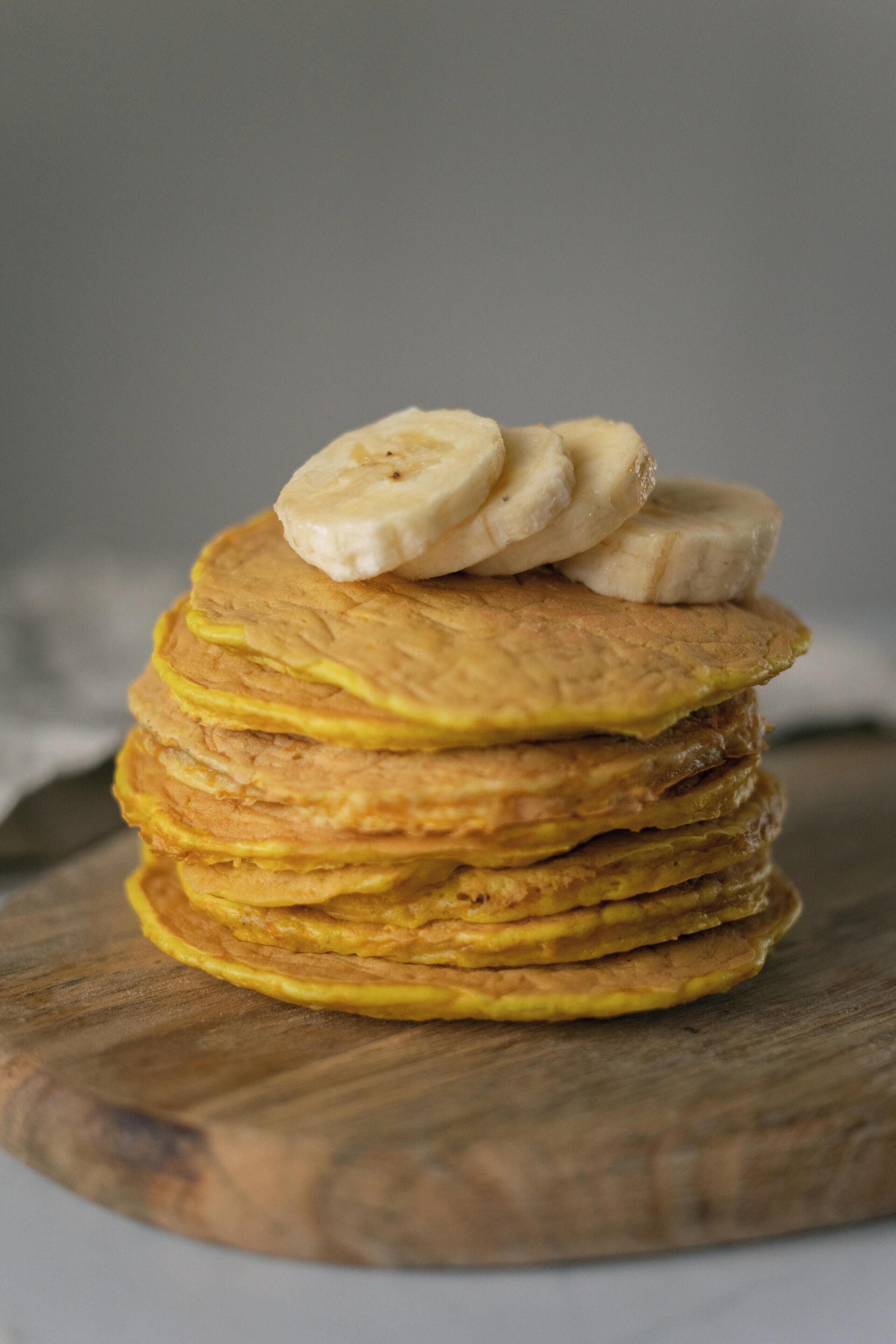 A stack of pancakes with banana slices on a wooden board.
