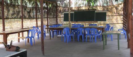 An indoor classroom with blue plastic chairs and tables, a blackboard, and a giraffe head decoration on a table.
