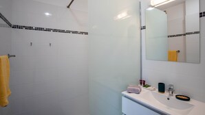 Uma casa de banho moderna com azulejos brancos, cabine de duche em vidro, lavatório branco e espelho.