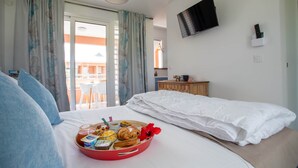 Quarto de hotel com cama, bandeja de café da manhã, televisão e varanda com cortinas.