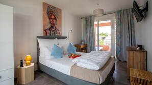 Quarto com cama, quadro, luminária, mesa de cabeceira, televisão e vista para o exterior.