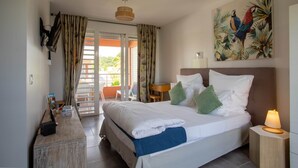 Ett väl upplyst hotellrum med en säng, ett skrivbord, en stol och en tavla som föreställer papegojor.