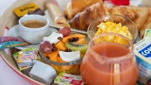 Ett frukostbricka med croissanter, äggröra, frukt, yoghurt och ett glas juice.