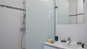 Een moderne badkamer met een douchecabine van glas, een witte wastafel met spiegel en een betegelde vloer.