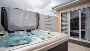 Un bain à remous doté d’un couvercle, une porte-fenêtre coulissante et un mur extérieur blanc.