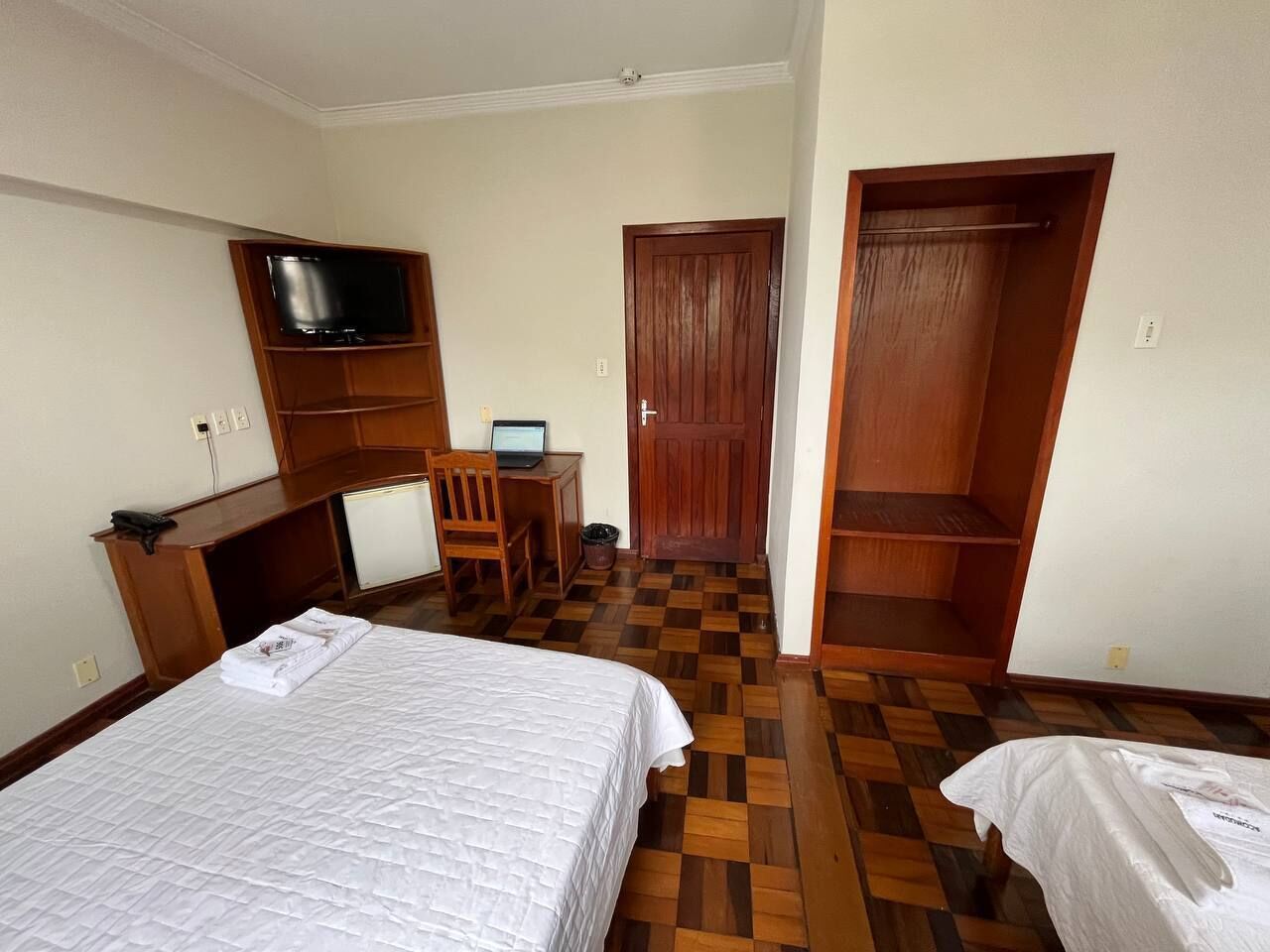 Habitación de hotel con cama, escritorio, computadora portátil, televisor y armario.
