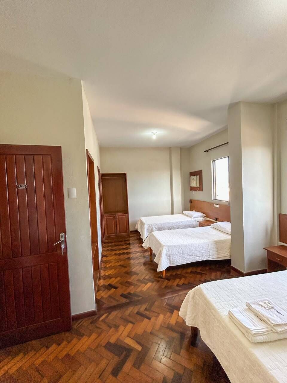 A hotel room with two beds, a wooden herringbone floor, a door with a number, and a window.