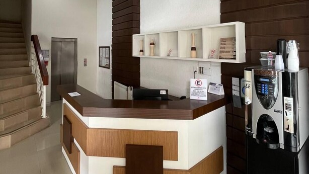 A reception area with a wooden reception desk, a coffee machine, and a staircase in the background. - ACOMODARE HOTEL (Tubarao)