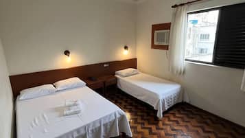 Quarto de hotel com duas camas, piso de parquet de madeira, janela com vista e luminária no teto.