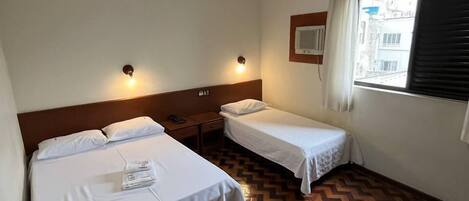 Habitación de hotel con dos camas, piso de parquet de madera, ventana con vistas y una luz en el techo.