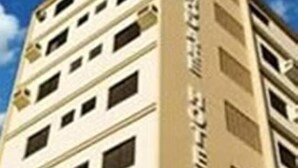 A multi-story hotel with a beige facade, multiple windows per floor, and a visible sign on the side. - ACOMODARE HOTEL (Tubarao)
