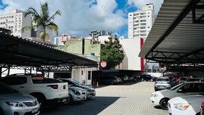 A parking area with multiple cars, a covered structure, and buildings in the background. - ACOMODARE HOTEL (Tubarao)