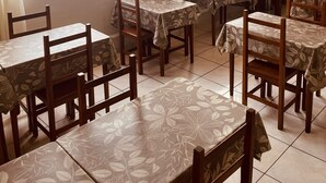 A dining area with tables and chairs, large windows with a view of a river and hills, and a kitchen area with a coffee machine. - ACOMODARE HOTEL (Tubarao)