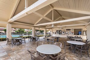 An outdoor patio area with multiple tables and chairs, a pool in the background, and a covered seating area with a ceiling fan. - KKSR#3103 DIRECT OCEANFRONT, INCREDIBLE OCEAN VIEWS & REMODELED! (Kailua Kona)