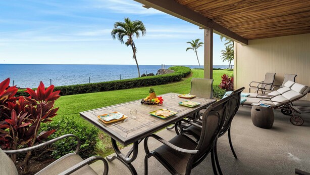 An outdoor dining area with a view of the ocean, a covered patio, and a seating area with lounge chairs.