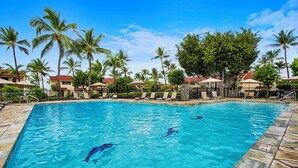 A swimming pool with clear blue water, surrounded by palm trees and lounge chairs.