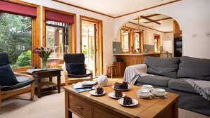 A cozy living room with a wooden coffee table, a grey sofa, and a dining table set with plates and a cake. - Langrick -  a bungalow that sleeps 10 guests  in 5 bedrooms (Nethy Bridge)