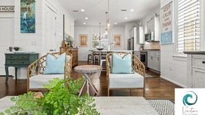 A spacious living room with two wicker sofas, a round coffee table, and a dining area with a chandelier. - Cabana Banana - 4 Bikes / 6-Seater Golf Cart (Santa Rosa Beach)