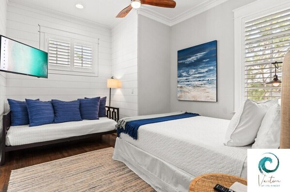 Un dormitorio con cama, sofá, un cuadro, ventilador de techo y televisor.