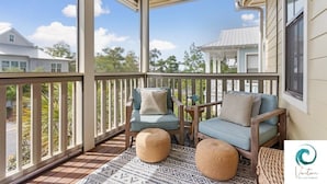 A covered porch with two blue cushioned chairs, a woven ottoman, and a patterned rug. - Cabana Banana - 4 Bikes / 6-Seater Golf Cart (Santa Rosa Beach)