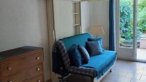 A room with a blue sofa, a wooden dresser, and a sliding door leading to a balcony. - Studio Climatisé Possibilité 4 Adultes/parking Privé (grasse)