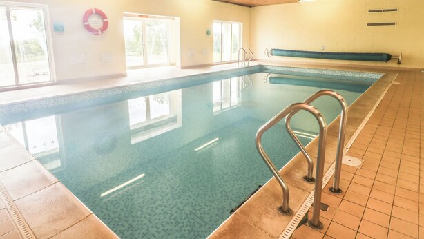 Ein Hallenbad mit klarem Wasser, einem Rettungsring und einer Sitzbank.
