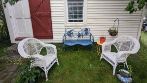 Un petit espace extérieur aménagé avec deux chaises en osier blanc et un banc en métal bleu.