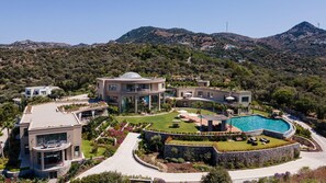 Una villa moderna con una gran piscina, varias habitaciones para huéspedes y un jardín ajardinado.