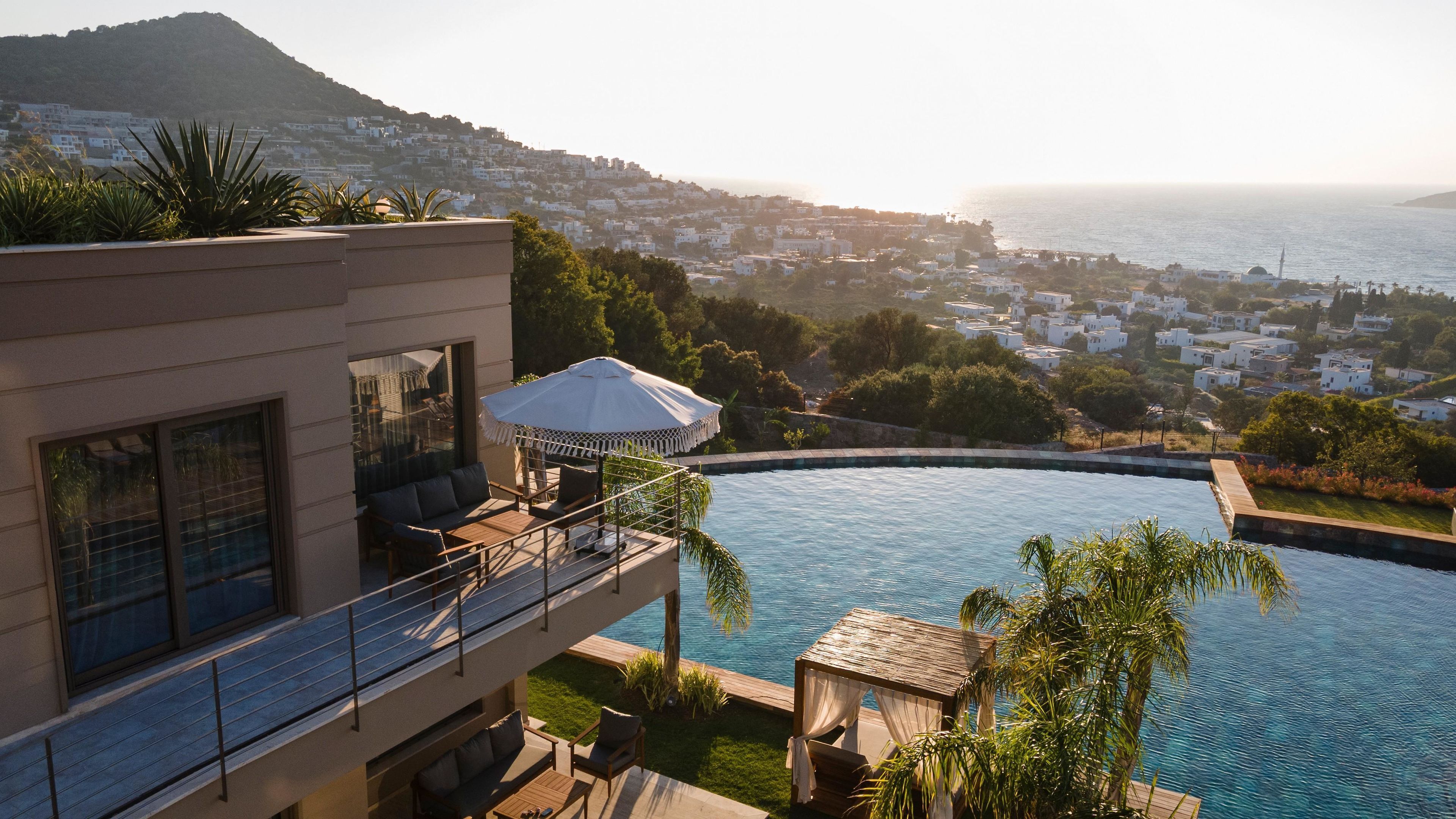 A modern building with a rooftop pool, outdoor seating, and a view of a coastal town.